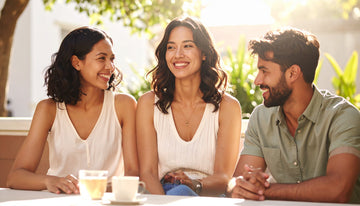 Three friends sitting together at a table outdoors, smiling and enjoying each other's company.